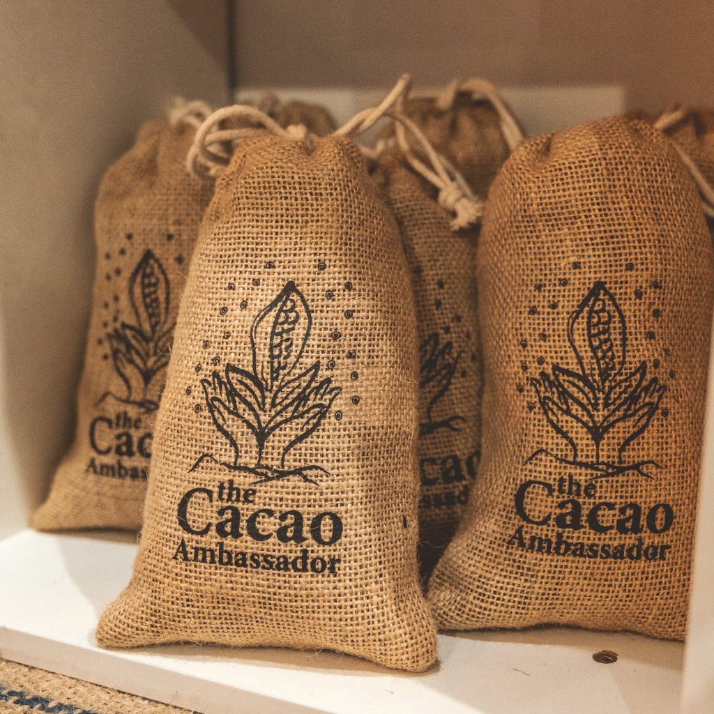 Jute bags with 'The Cacao Ambassador' branding on a shelf.