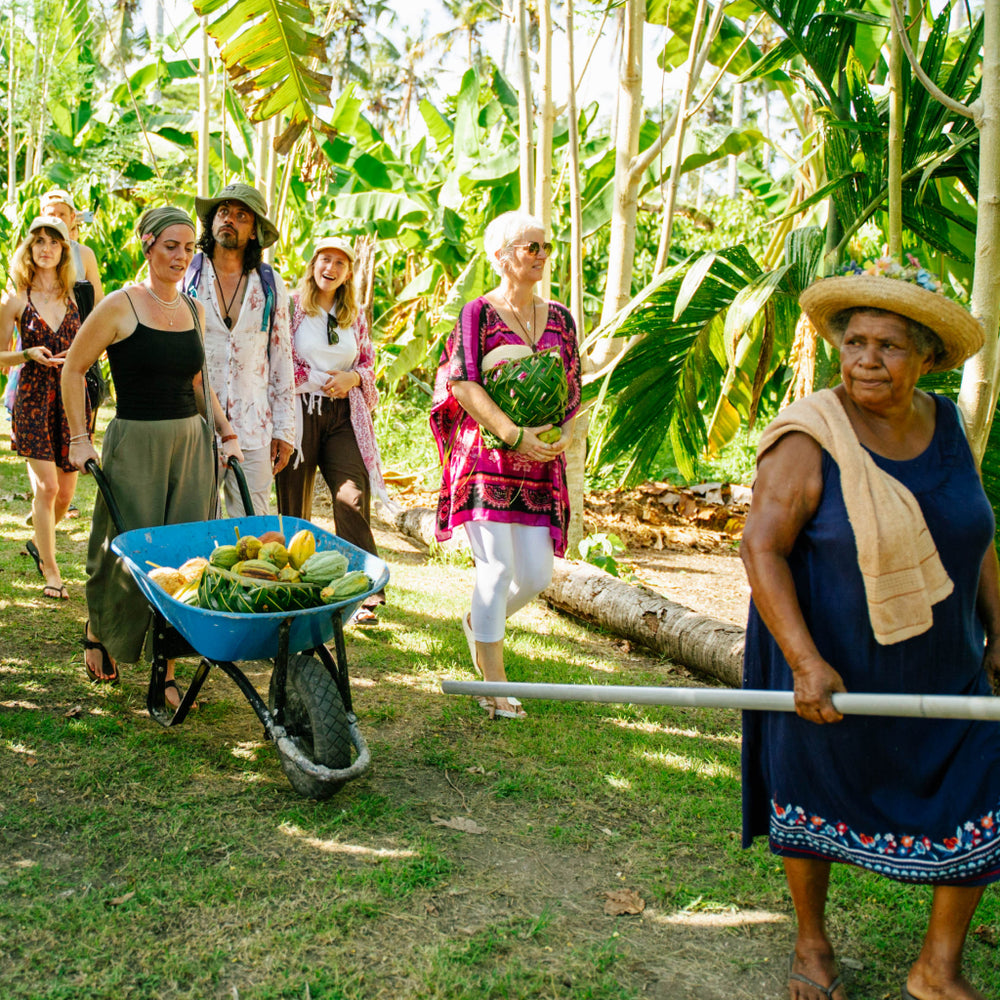 Group of people on a cacao farm with a woman pushing a wheelbarrow full of cacao pods.