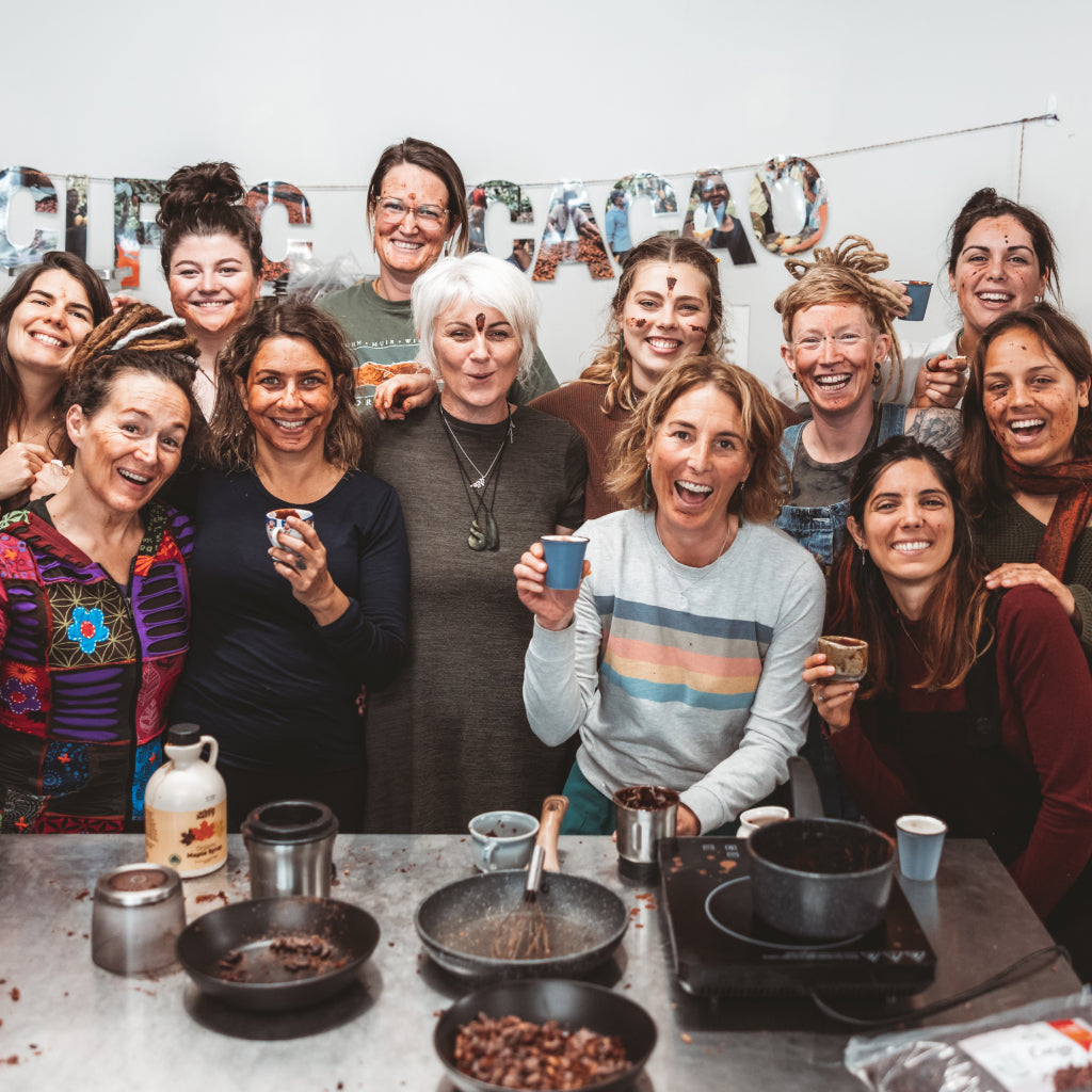 Group of people posing together in a kitchen with cacao-making equipment.