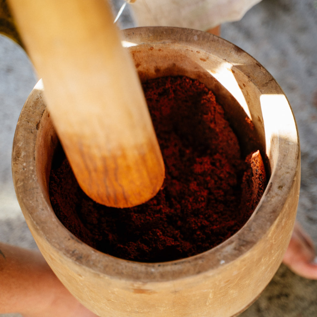 Wooden pestle grinding cacao powder in a wooden mortar.